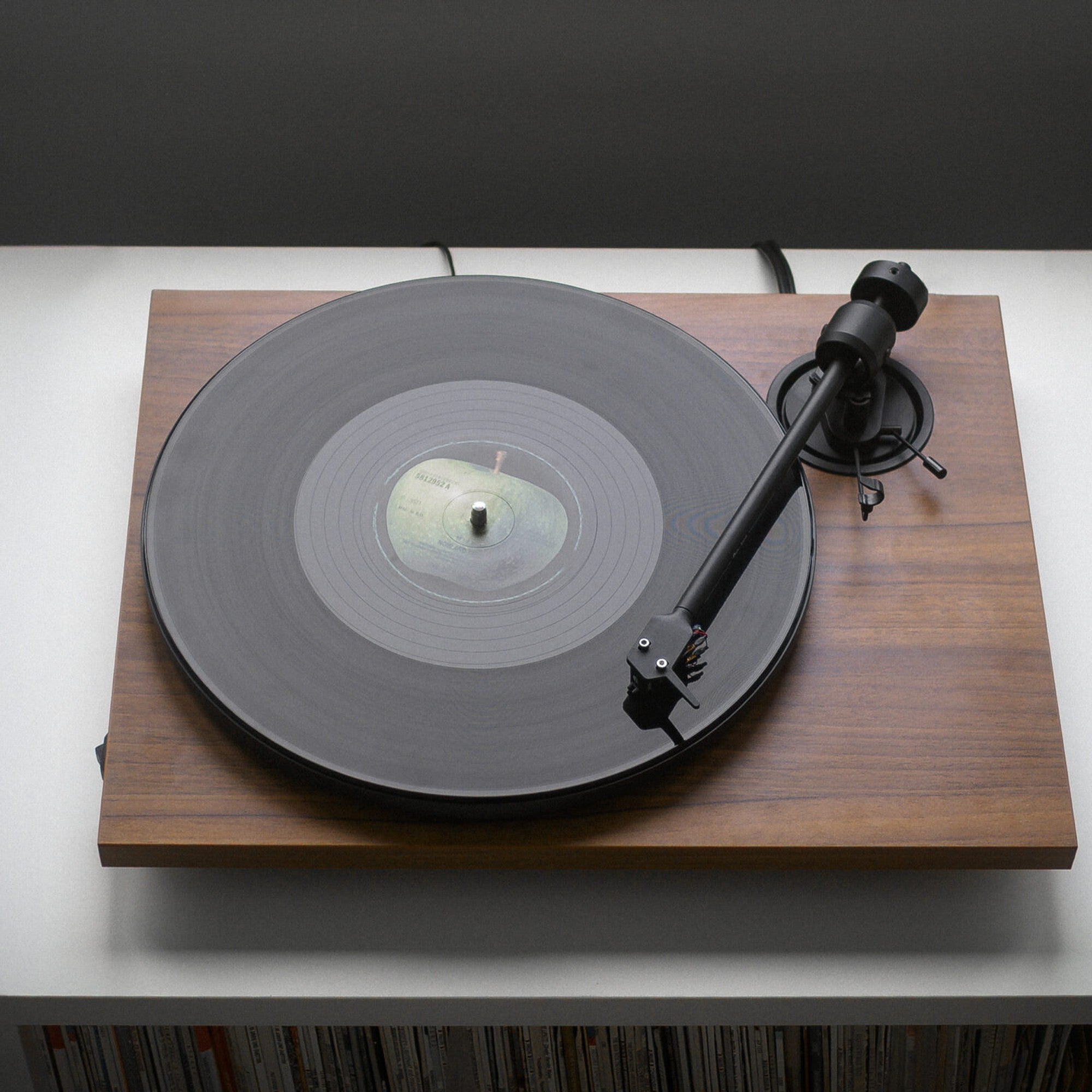 Pro-Ject E1.2 BT in walnut playing a record on a console above a row of vinyl