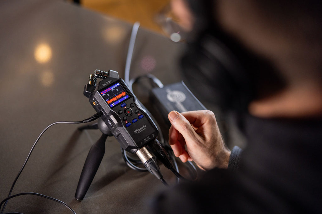 Zoom H4essential digital recorder shown in a lifestyle setting with microphones and accessories.