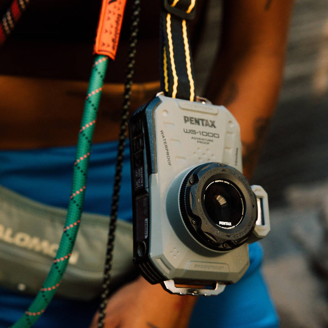 Ricoh Pentax WG-1000 compact instant camera with waterproof design, shown in a vibrant outdoor setting.