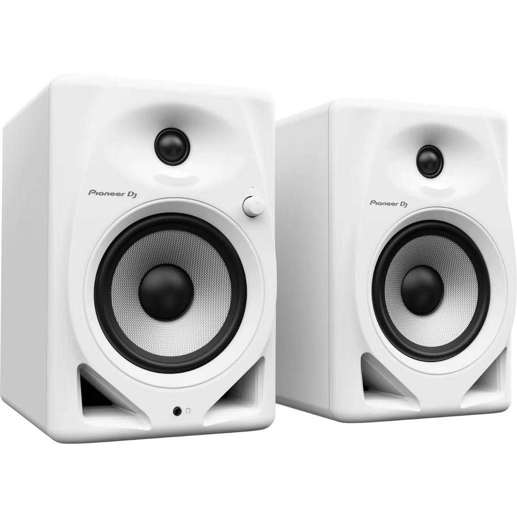 Pioneer DJ DM-50D desktop speakers shown on a desk with audio equipment in the background.