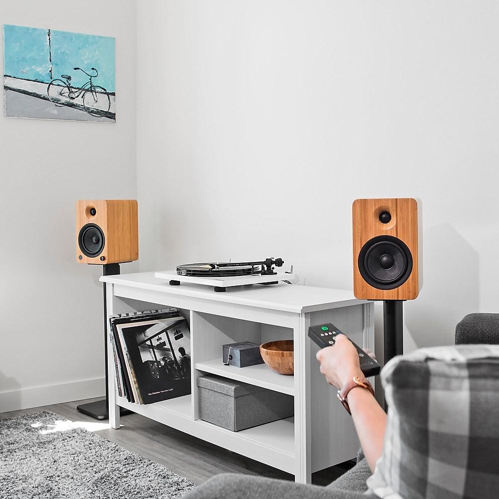 Kanto Audio SP26 26-inch speaker stands holding two speakers on a wooden floor with a beige wall background.