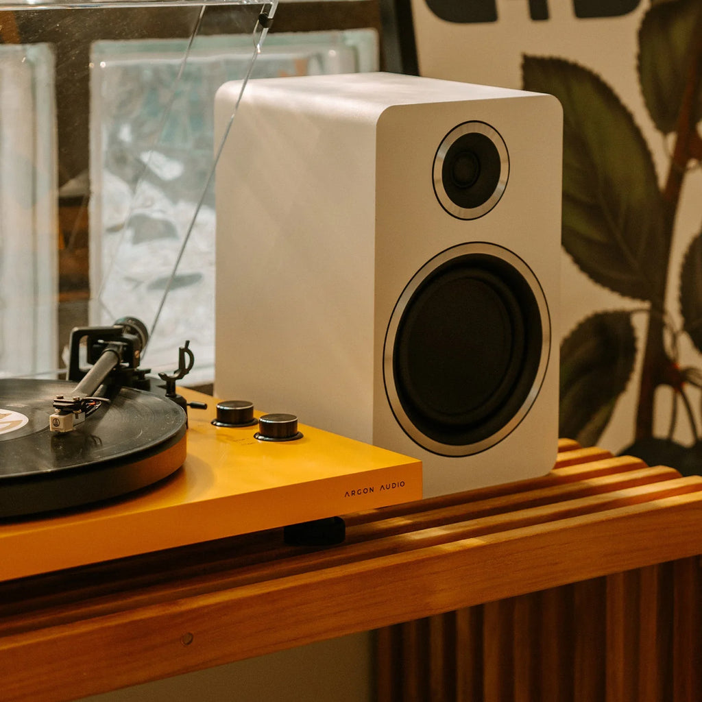 Argon Audio Fenris A5 active bookshelf speakers with white enclosures and black speaker grilles, placed on a wooden surface.