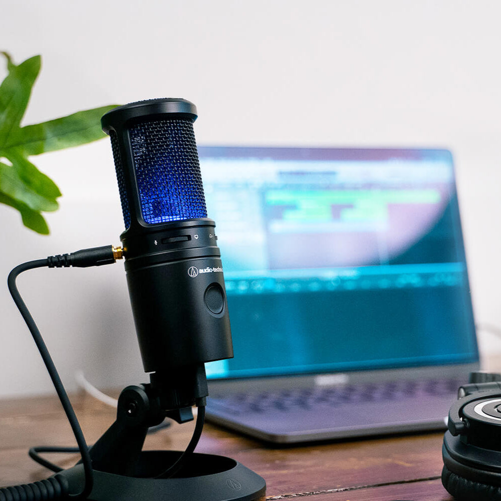 Audio Technica AT 2020 USB-X microphone on a desk with a computer, showcasing a professional USB microphone setup for streaming or recording.