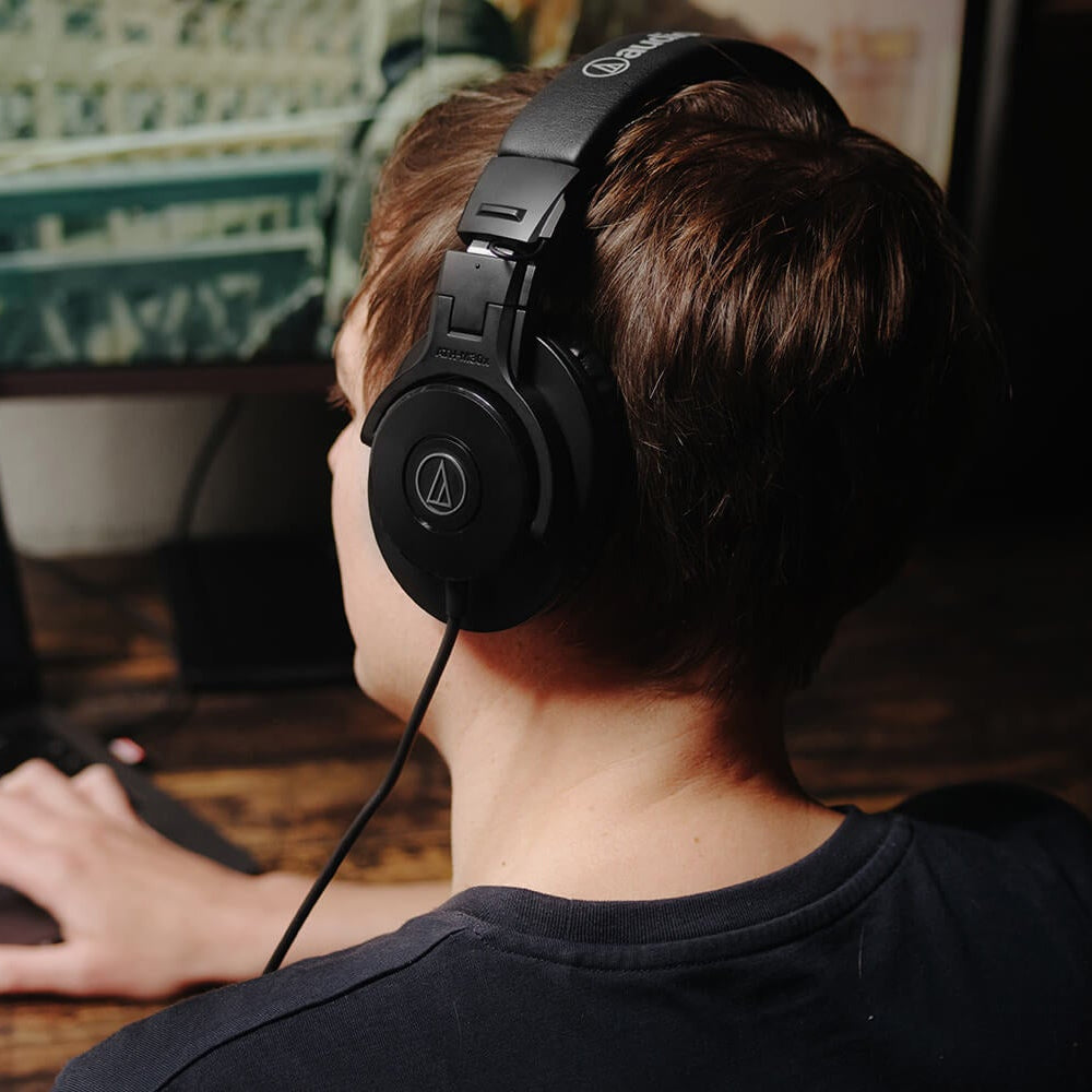 Audio Technica ATH-M30x studio headphones resting on a desk with a laptop and audio equipment in a professional music studio setting.