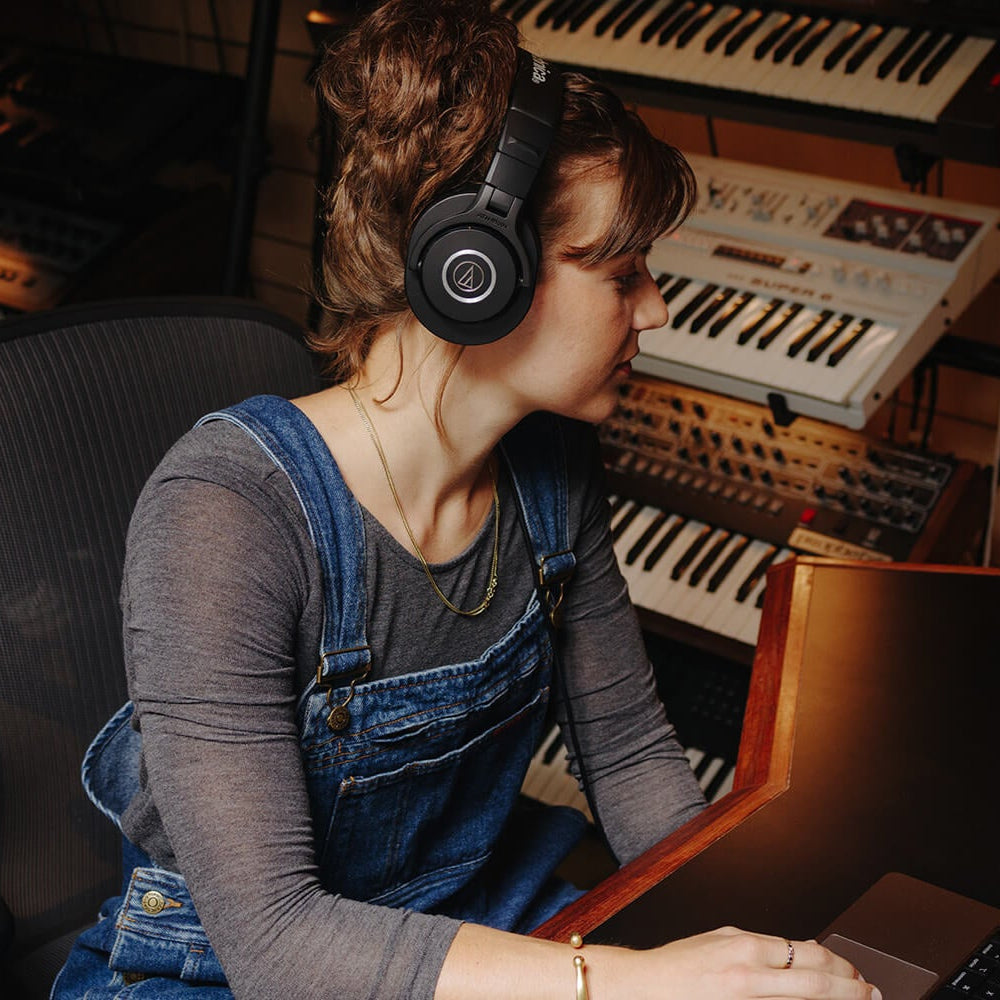 Audio Technica ATH-M40x studio headphones shown in a lifestyle setting on a desktop, featuring over-ear design and professional audio quality.