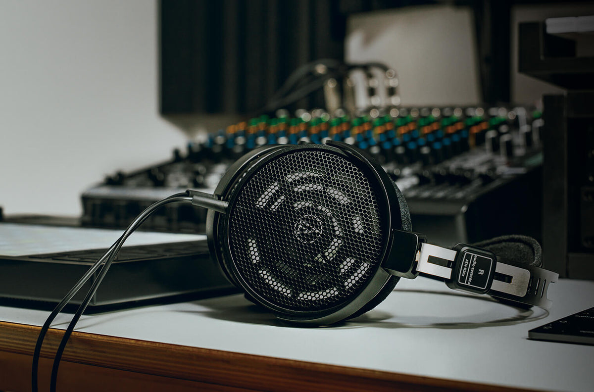 Audio Technica ATH-R30x studio headphones shown in a lifestyle setting with a modern workspace and open-back design.