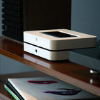 Bluesound Powernode 2025 music streamer in white with a turntable, showcasing compact design and audio equipment setup.