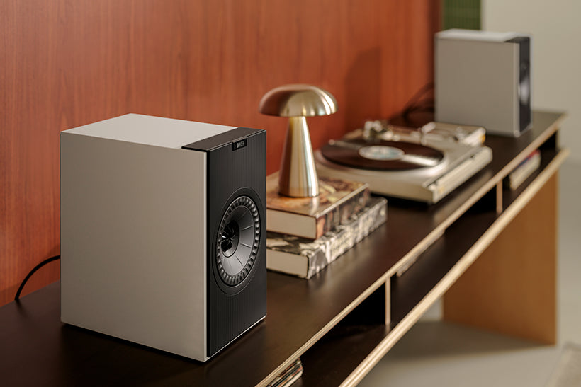 KEF Coda W active bookshelf speakers in nickel grey finish, shown in a modern living room setting with vinyl record and CD.