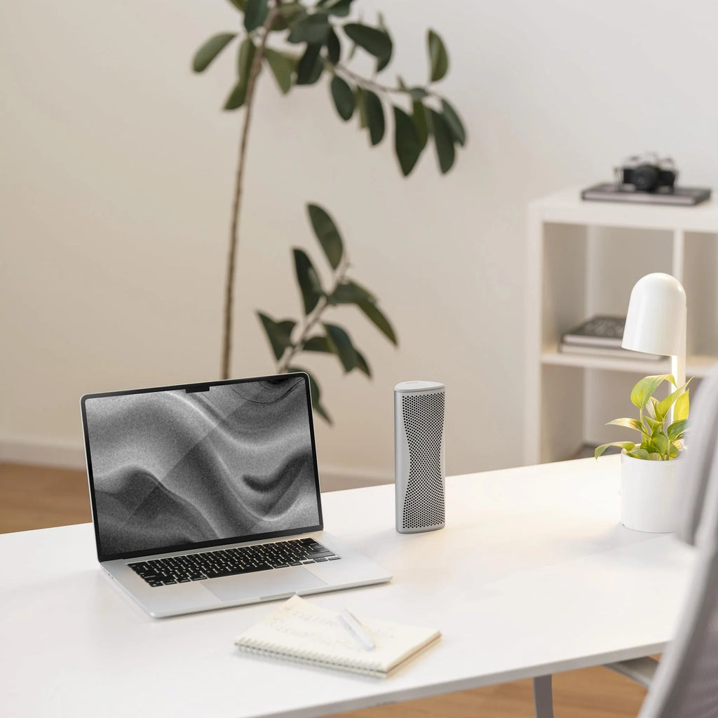 Silver KEF Muo portable speaker with a sleek design, shown next to a laptop, delivering high-quality sound.