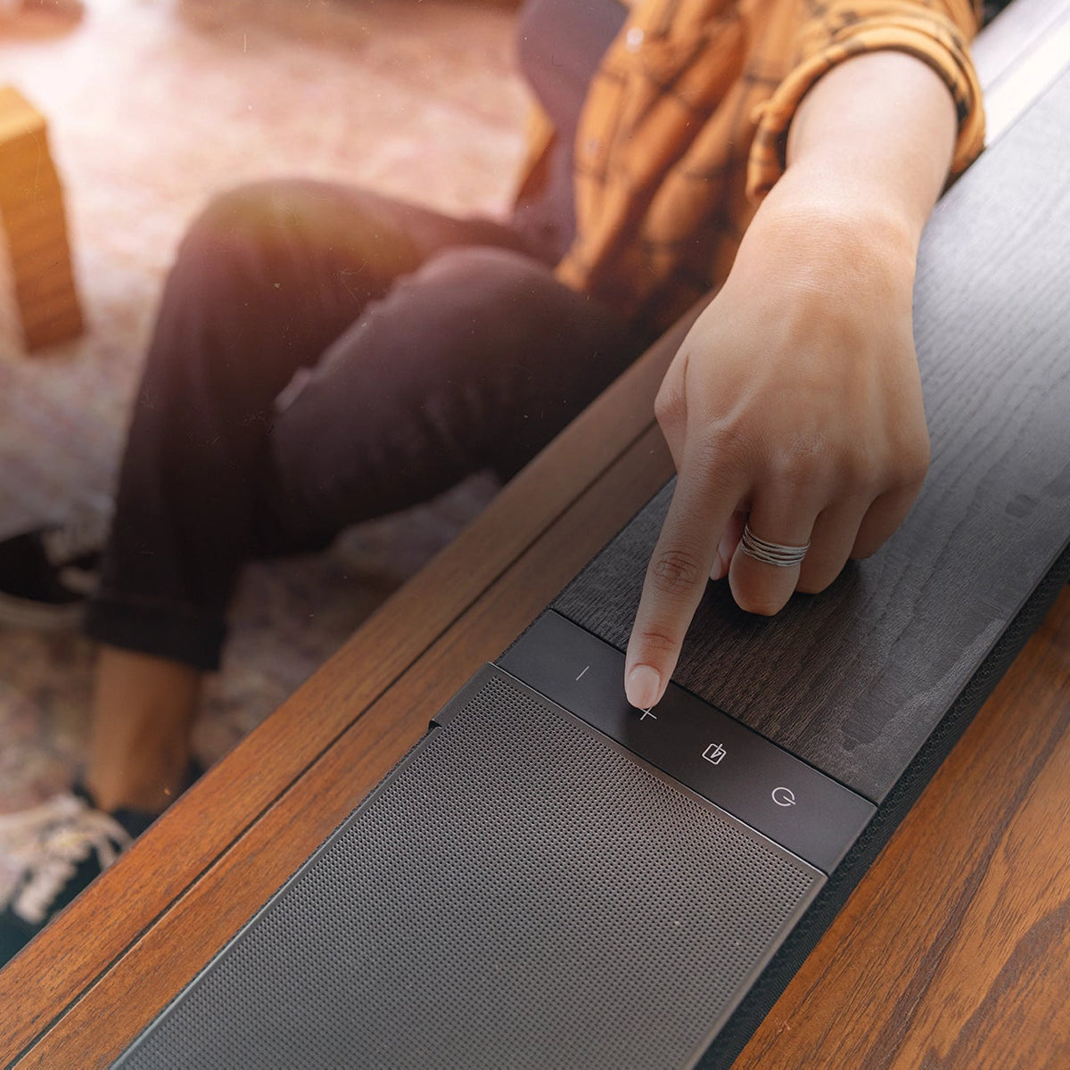 Woman pressing button on Klipsch Flexus Core 300 soundbar, sleek black TV speaker with modern design.