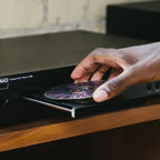 NAD C 589 CD player with hand adjusting controls, close-up view showing front panel and disc tray.