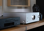 Onkyo Icon A-50 silver stereo amplifier beside Klipsch bookshelf speaker with wall art in the background.