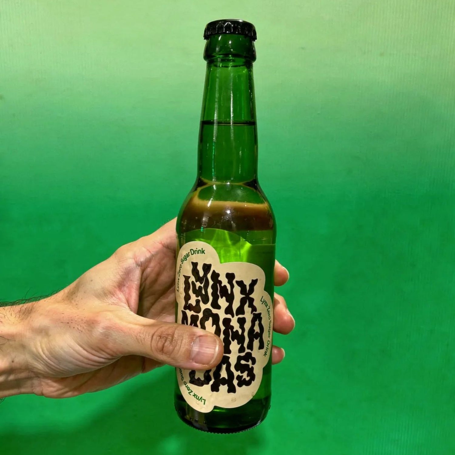 Hand holding a green bottle with a label against a green background