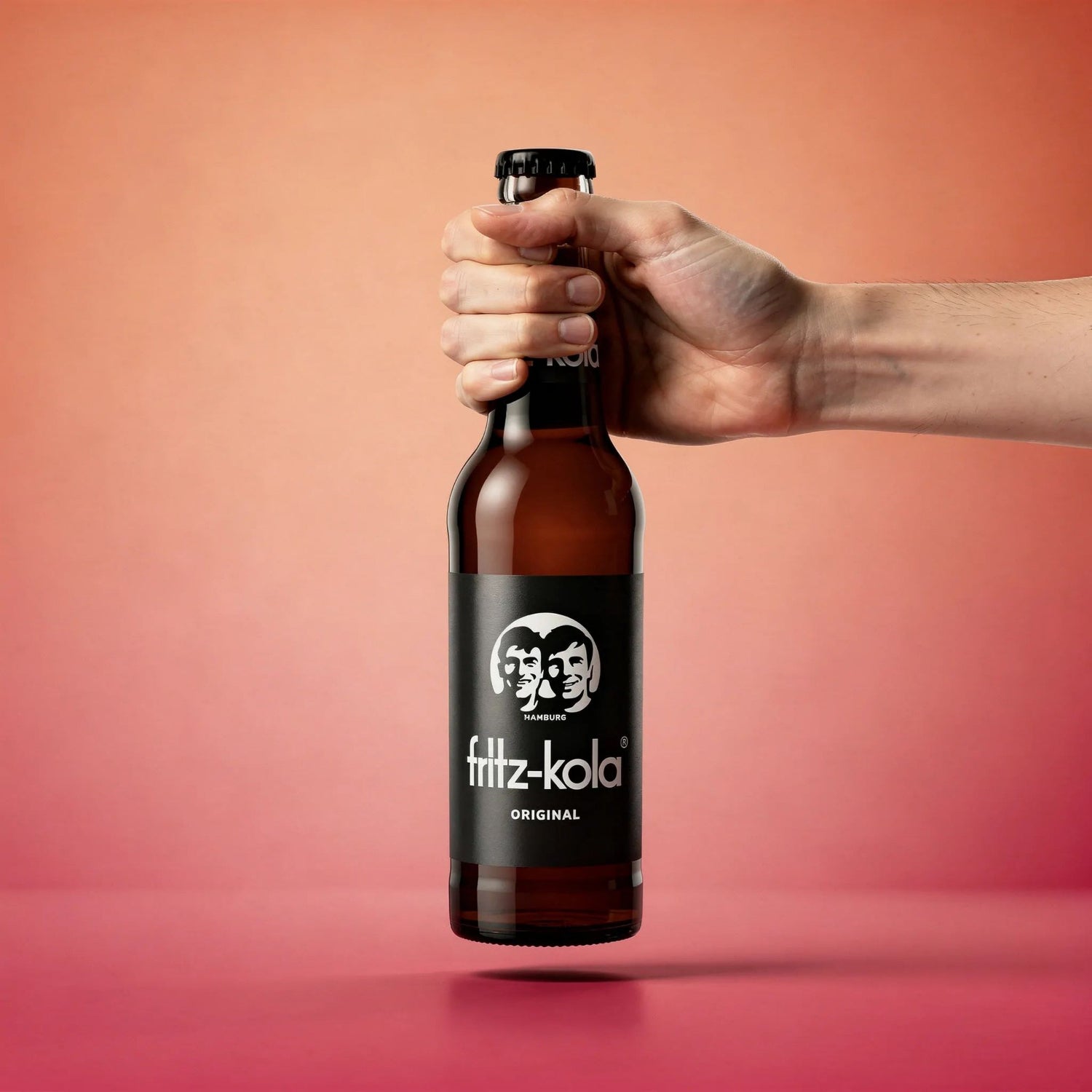 Hand holding a bottle of fittz-kola against a gradient background