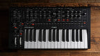 Moog Messenger synthesizer with black and silver design, featuring various knobs and buttons on a sleek electronic music device.