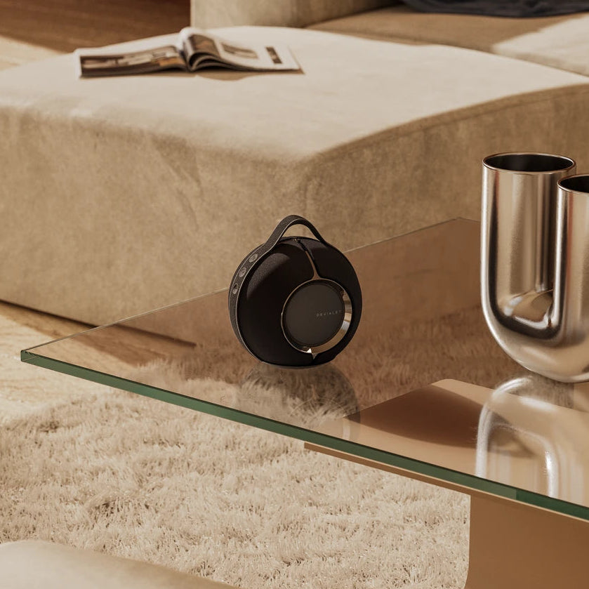 Devialet Mania portable speaker in deep black, shown in a lifestyle setting with a sleek, modern design and compact size.