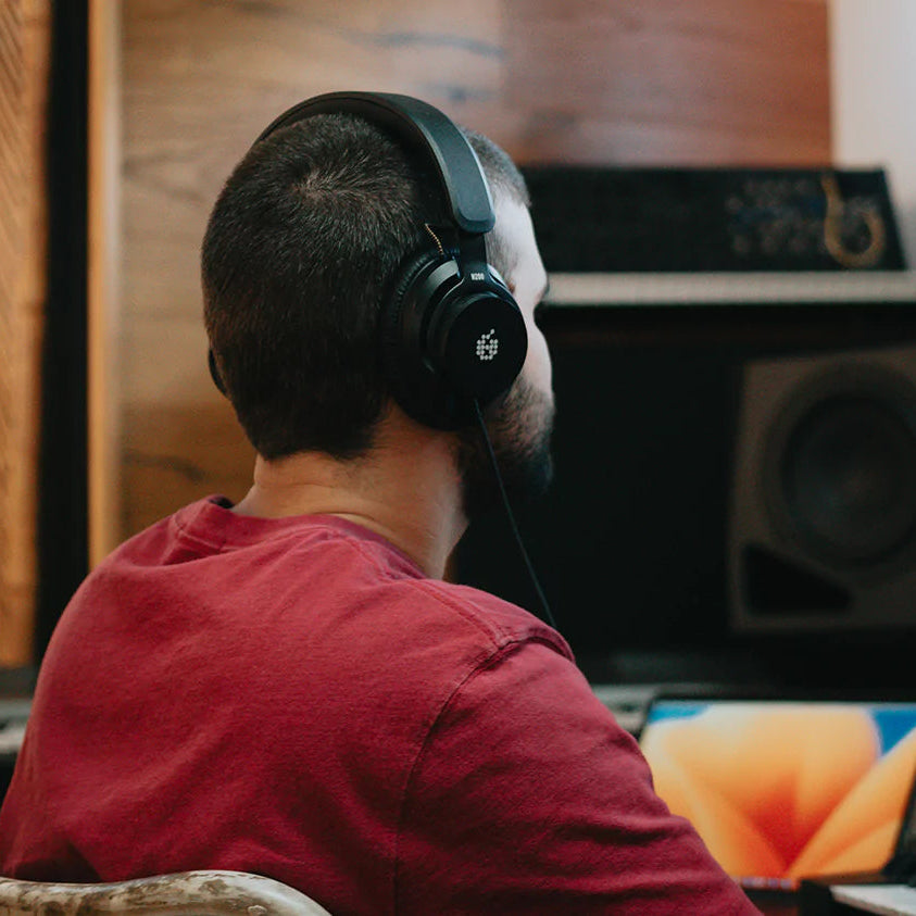 Adam Audio H200 studio headphones shown resting on a desk with a sleek black design and padded ear cups for comfortable listening.