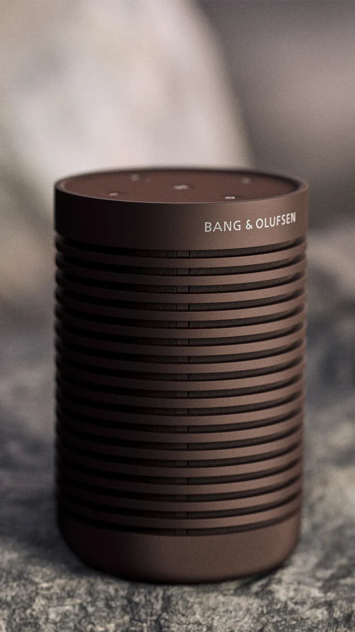 Bang & Olufsen Beosound Explore portable speaker in chestnut color, showing its cylindrical design and textured fabric exterior.