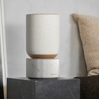 Bang & Olufsen Beosound Balance wireless speaker in a sleek, modern design with a fabric cover and wooden base.