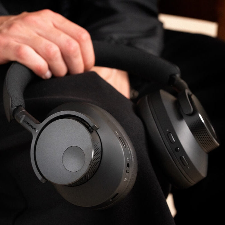 Black Cambridge Audio Melomania P100 SE wireless headphones held in hand, showcasing compact design and sleek finish.