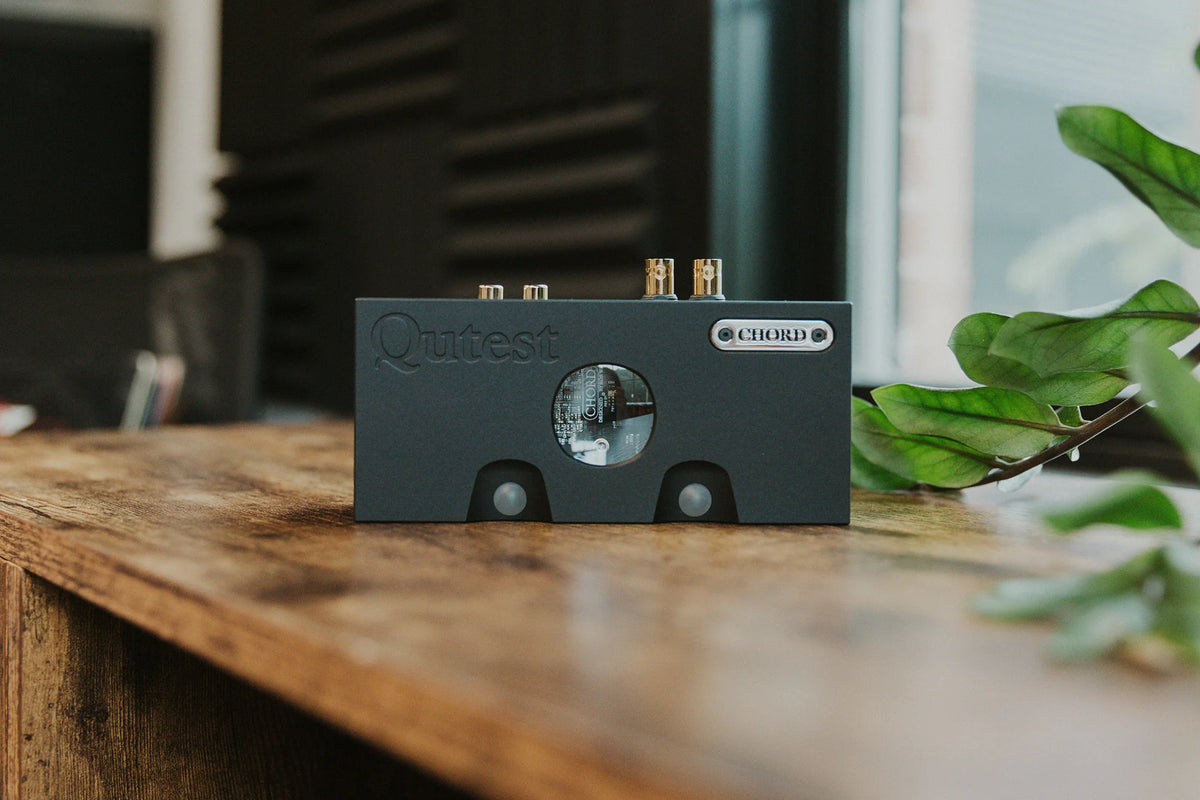 Chord Electronics Qutest headphone amplifier and DAC, compact device with sleek design, shown in a modern lifestyle setting.