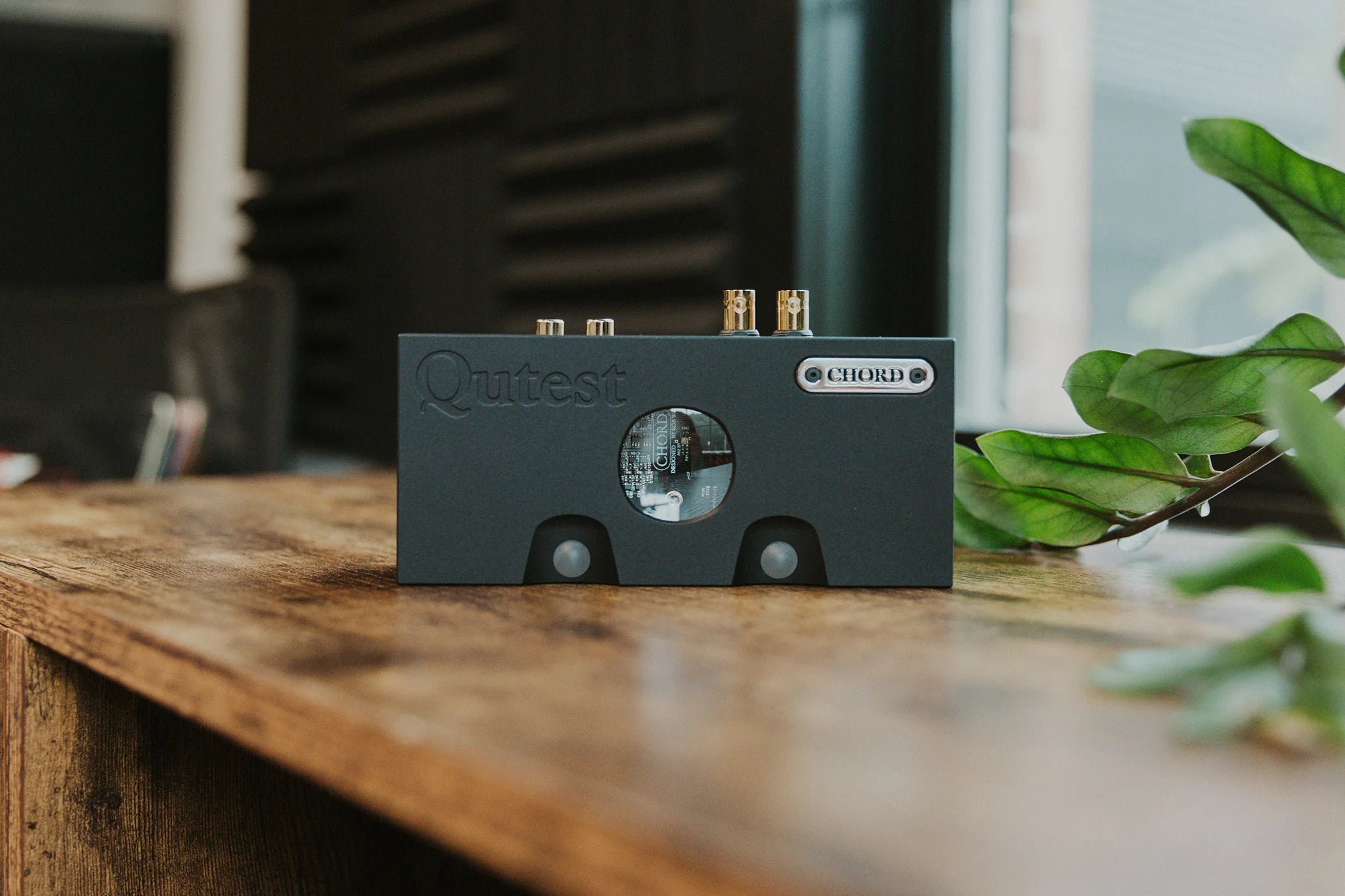 Chord Electronics Qutest headphone amplifier and DAC, compact device with sleek design, shown in a modern lifestyle setting.