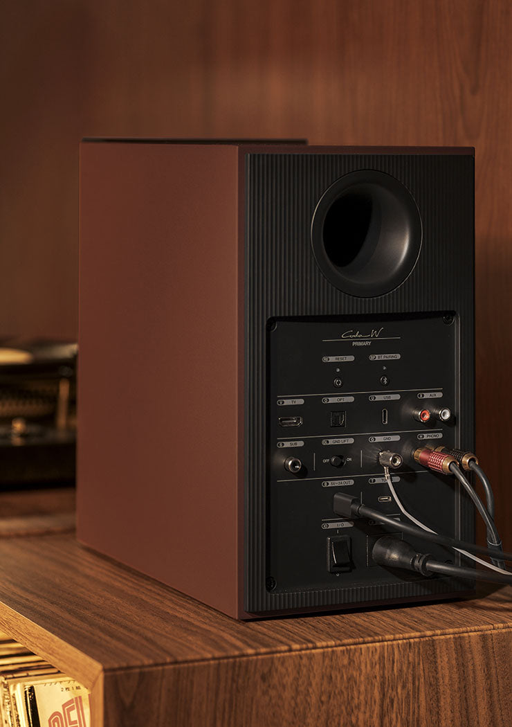 KEF Coda W active bookshelf speakers in vintage burgundy finish, shown in a lifestyle setting with audio connections.