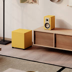 Dali Basik Sub in Golden Yellow next to a matching bookshelf speaker in a living room