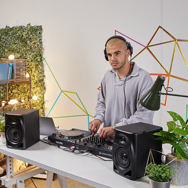 Pioneer DJ DM-50D desktop speakers shown in a stylish home setup with modern decor and electronic equipment.
