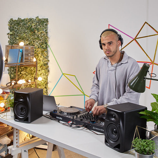 Pioneer DJ DM-50D-BT desktop speakers set up on a desk with a laptop and audio equipment, showcasing their compact design and controls.
