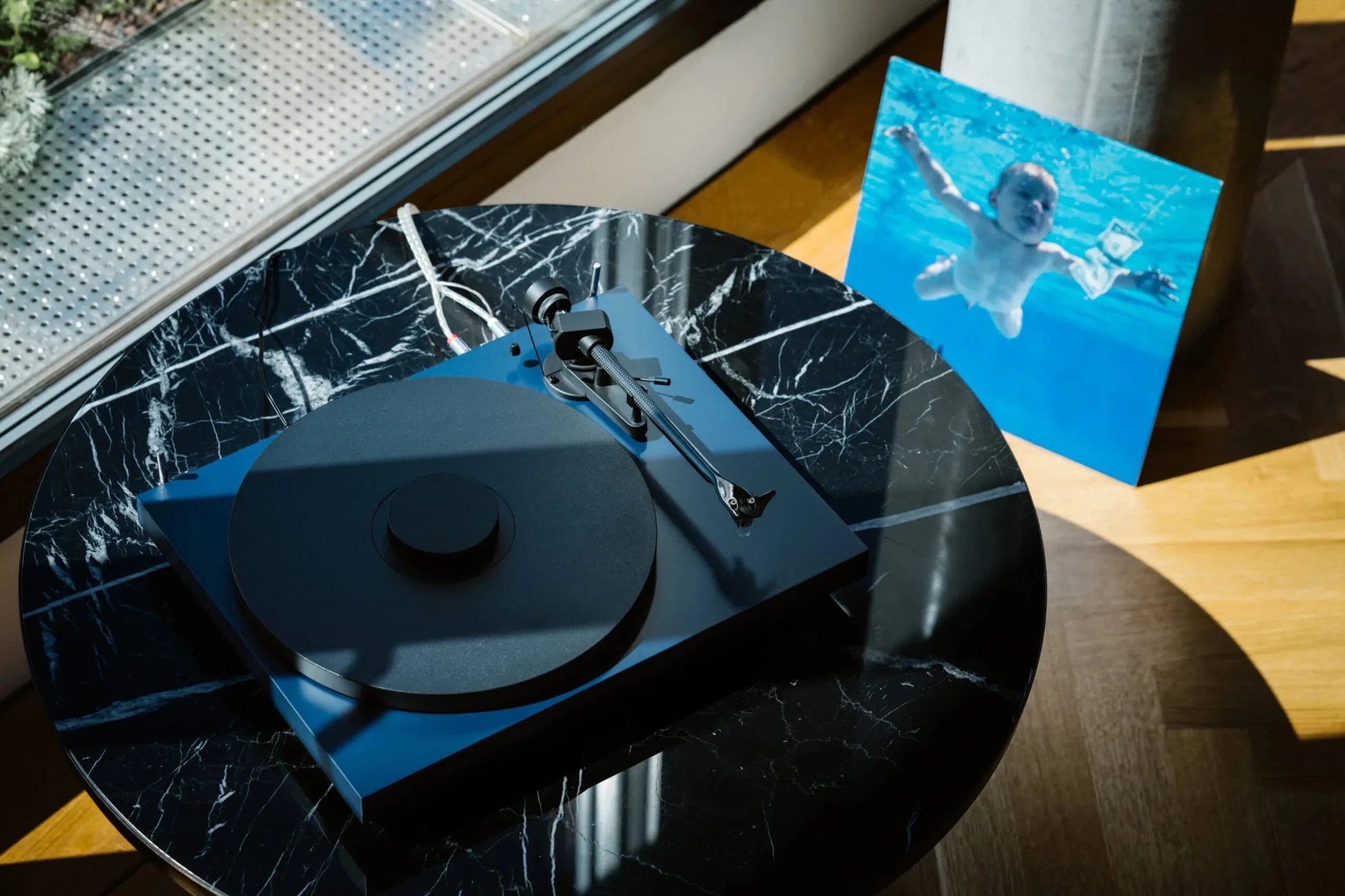 Pro-Ject Debut EVO 2 turntable in satin steel blue, shown in a modern loft lifestyle setting.