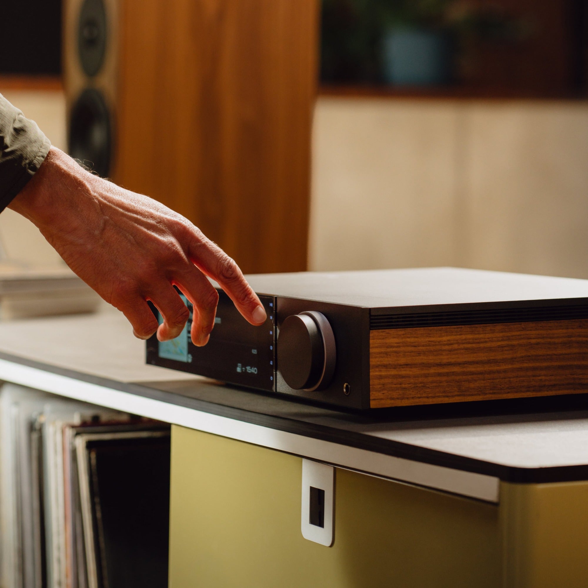 Cambridge Audio Evo 300 in use — adjusting the volume dial in a living room above a vinyl collection