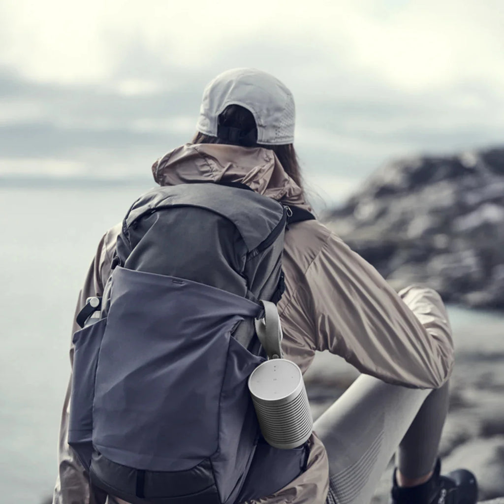 Woman holding the Bang & Olufsen Beosound Explore portable speaker, showcasing its compact design and rugged outdoor features.