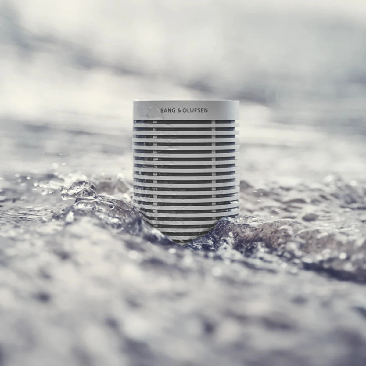 Bang & Olufsen Beosound Explore portable speaker submerged in water, showcasing its waterproof and rugged design.