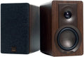 DALI Kupid passive bookshelf speakers shown in a modern living room setting, highlighting their sleek black design and compact size.