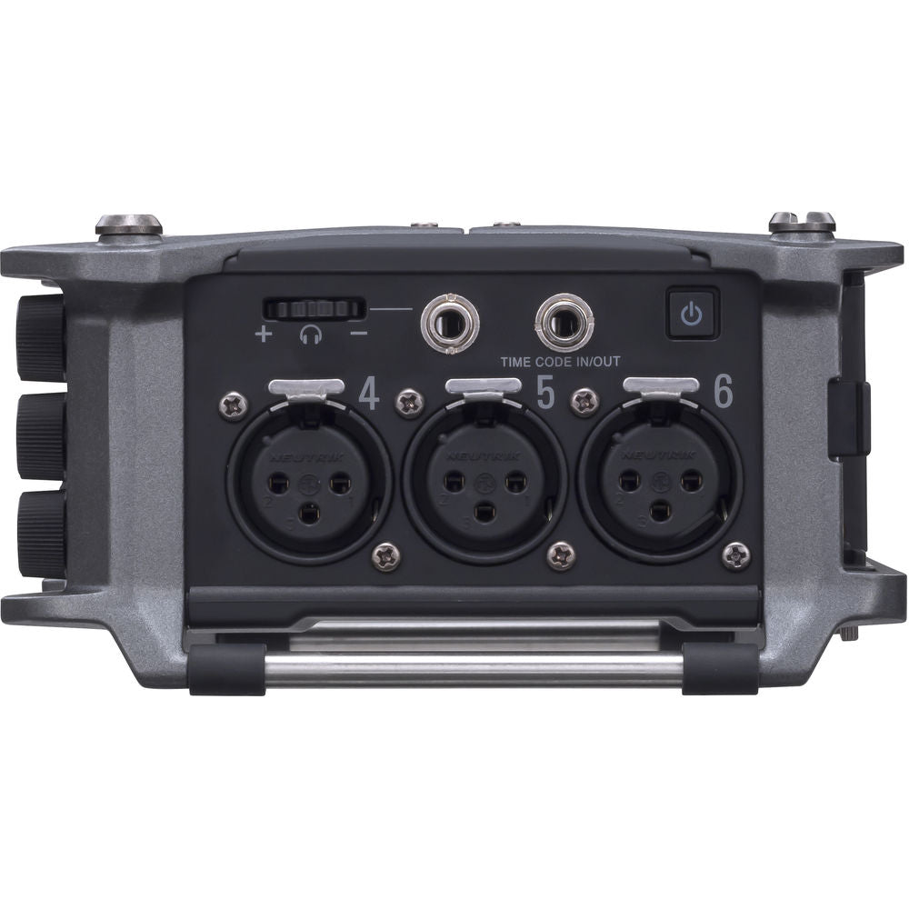 Zoom F6 digital recorder with multiple input jacks and LCD display, shown on a table with various cables and accessories.