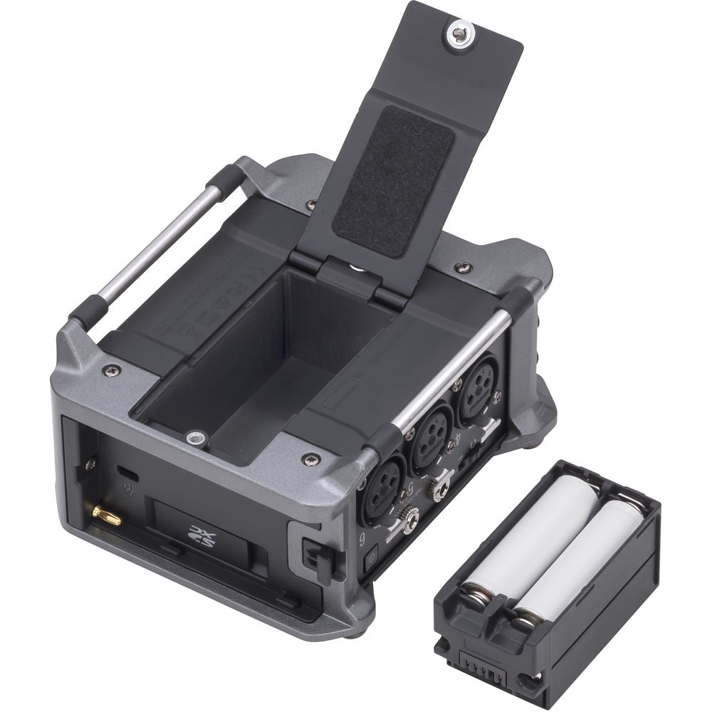 Zoom F6 digital recorder with multiple input jacks and LCD screen, shown on a table with accessories.