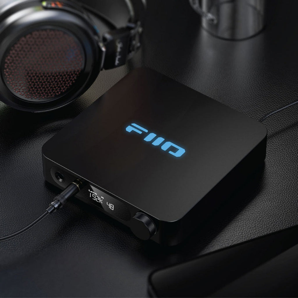 FiiO K11 black headphone amplifier and DAC with sleek design, shown on a lifestyle setup with cables and audio equipment.