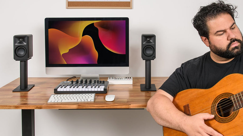 Kanto Audio Ora desktop speakers on a musician's desk with audio equipment and a laptop in a modern workspace.