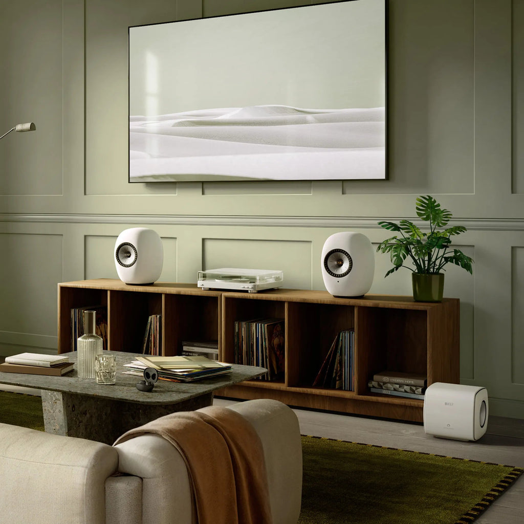 KEF LS Luxe in Mineral White on a walnut credenza with a wall-mounted TV and KEF subwoofer