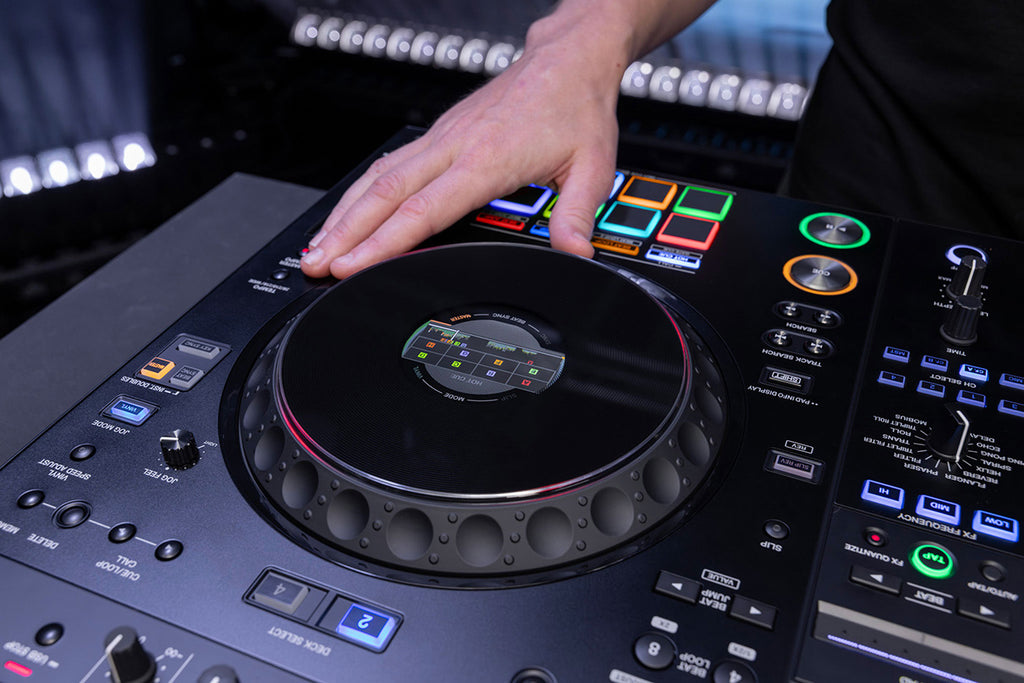 AlphaTheta XDJ-AZ DJ media player in a DJ setup with turntables, mixer, and headphones on a professional DJ stage.