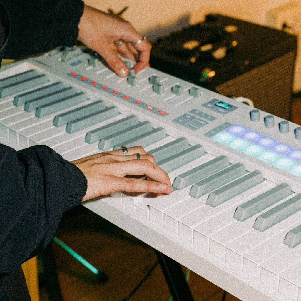 Novation Launchkey 49 MK4 MIDI keyboard with white casing, featuring keys and control knobs, set in a music studio environment.