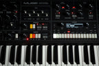 Moog Muse synthesizer with sleek black design featuring knobs and controls, displayed on a black background.