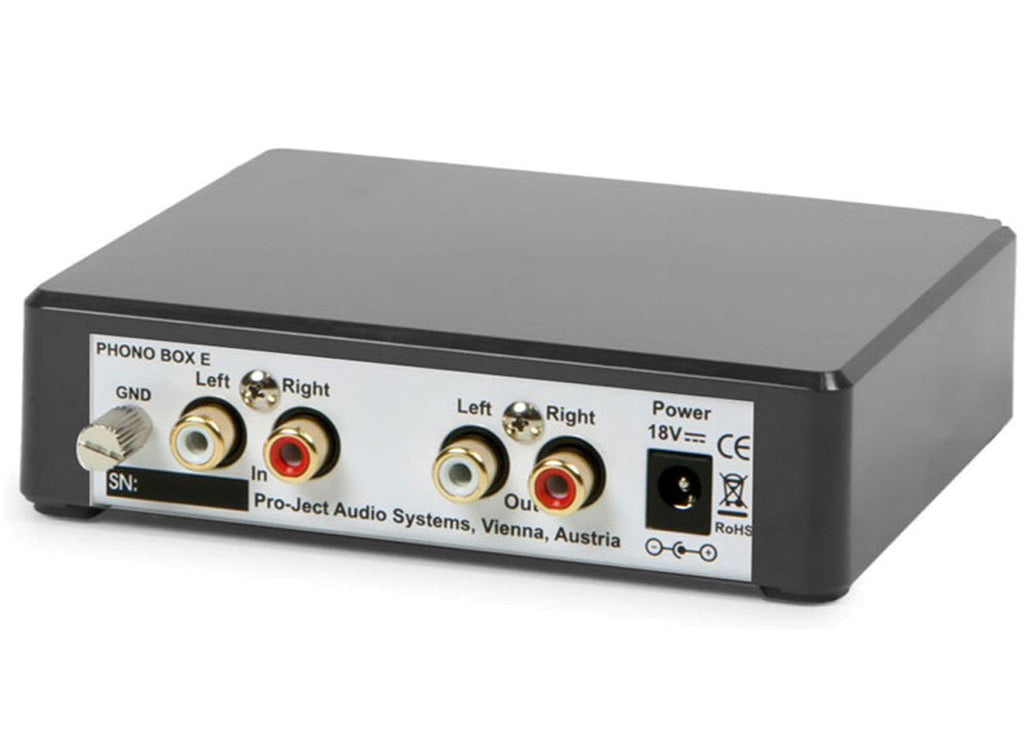 Pro-Ject Phono Box E phono preamp sits on a wooden surface, featuring input and output connections for high-quality audio amplification.
