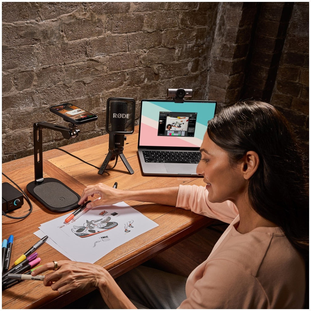 Rode DS3 black desktop studio arm on a wooden desk beside a laptop during a remote work session