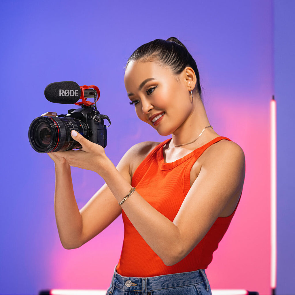 Rode VideoMic Go II shotgun microphone mounted on a camera in a neon-lit room with a person shooting a video.
