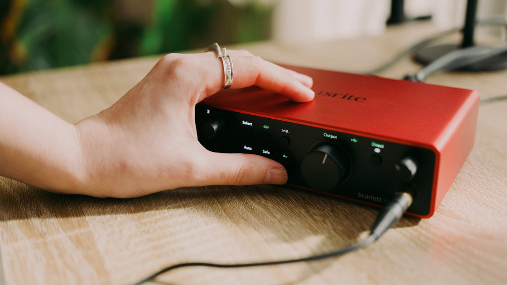 Focusrite Scarlett 2i2 4th Gen audio interface with dual microphone inputs and control knobs, placed on a desk with connected cables.